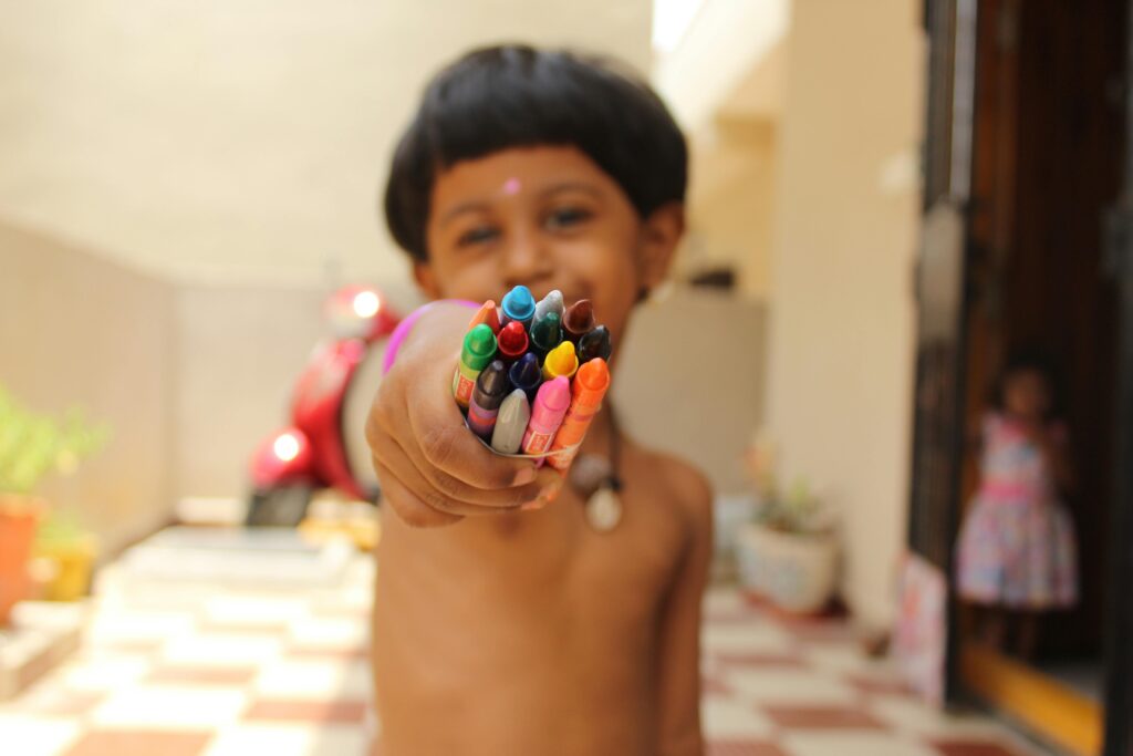 A happy child in Hyderabad proudly shows off a handful of vibrant crayons, capturing creativity's joy.